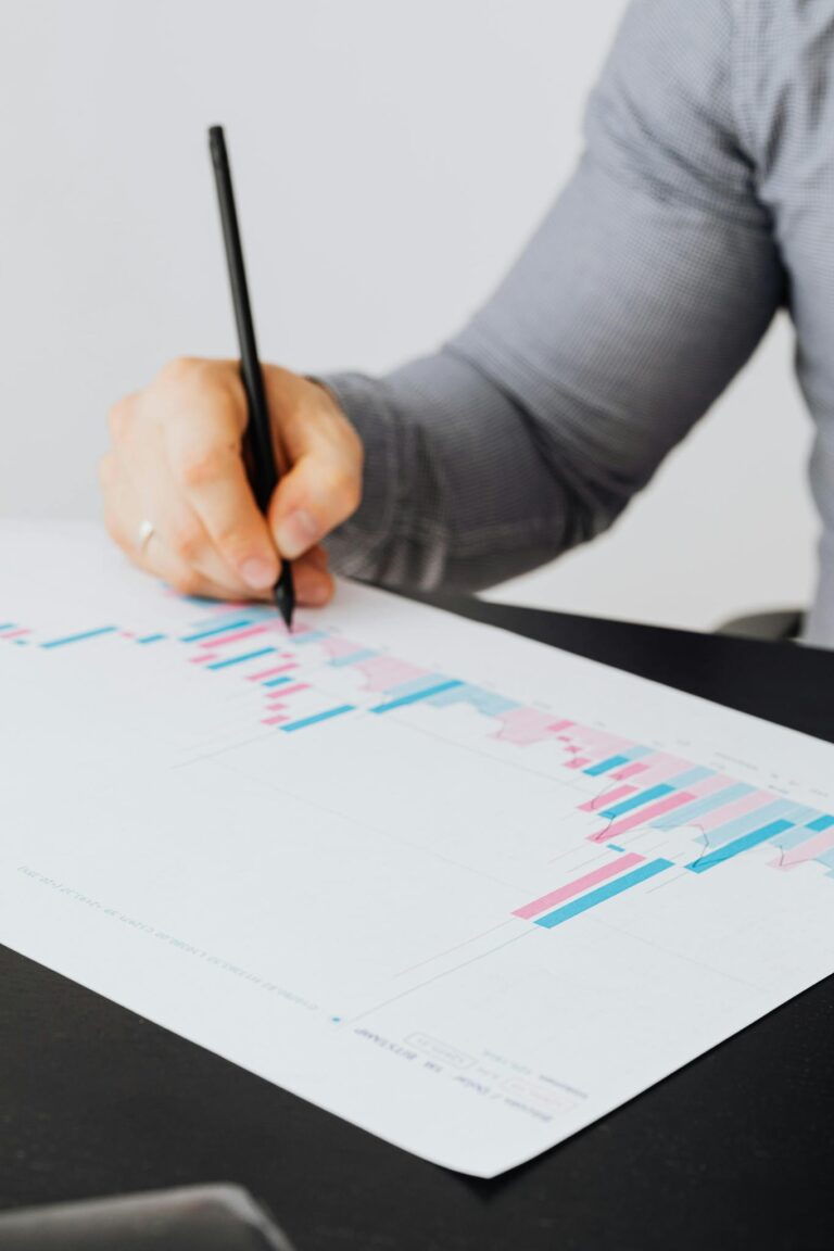 Person writing on a graph paper with colorful data bars and charts.